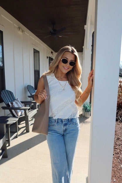A woman with long blonde hair in sunglasses smiles on a porch, wearing blue jeans and the Mika Ivory Ruffled Lace Top.