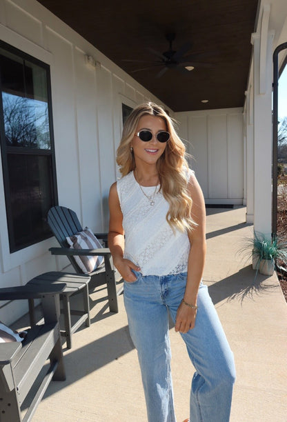 Woman with long blonde hair in sunglasses wears the Mika Ivory Ruffled Lace Top and blue jeans, standing on a sunny porch.