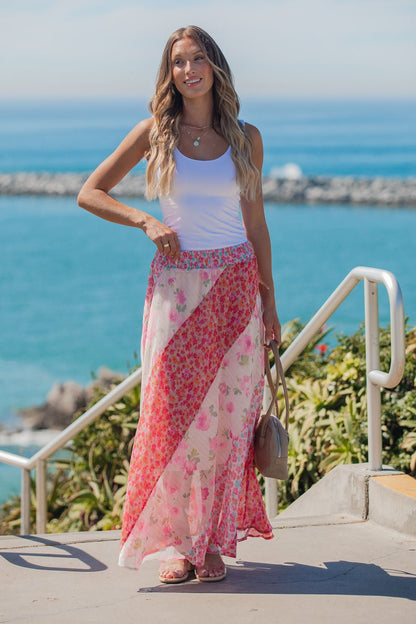Woman in a white tank and Mixed Print Smocked Maxi Skirt - Pink stands outdoors by the ocean, smiling on a sunny day.