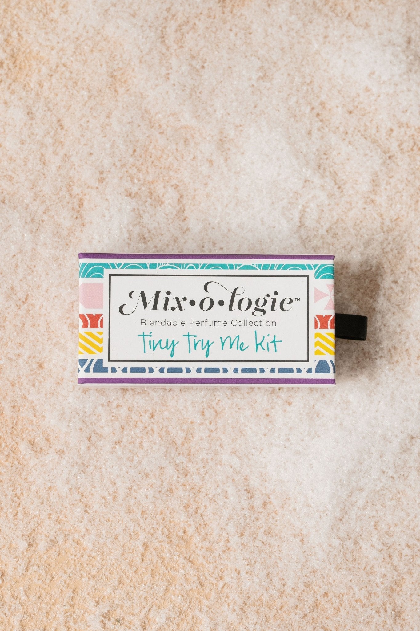 A Mixologie Tiny Try Me Perfume Kit box with customizable, alcohol-free perfume rests on a textured, neutral background.