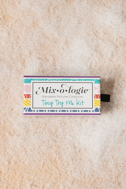 A Mixologie Tiny Try Me Perfume Kit box with customizable, alcohol-free perfume rests on a textured, neutral background.