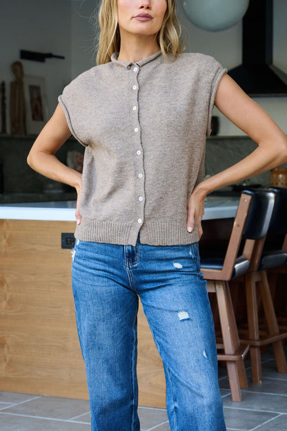 A woman wears a Mocha Cap Sleeve Button Down Top and blue ripped jeans, standing indoors with her hands on her hips.