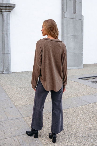 A woman wears a Mocha Collared High Low Pullover, wide-leg black jeans, and boots, standing outdoors with her back to the camera.