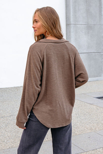 Woman with long hair in a Mocha Collared High Low Pullover and black jeans, standing outside with her back to the camera.