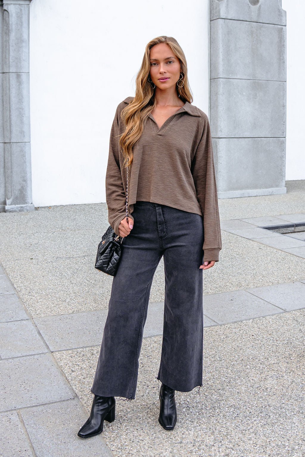 Woman in a Mocha Collared High Low Pullover, black wide-leg jeans, and boots stands on a city sidewalk with an oversized fit.