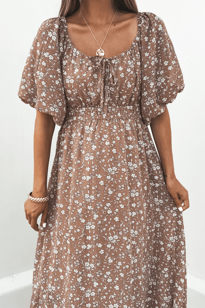 A woman wears the Mocha Floral Print Smocked Midi Dress with puff sleeves and a gold necklace, standing against a white background.