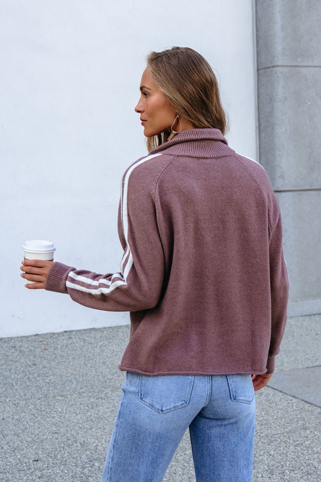 Woman with long hair wears the Mocha Half Zip Collared Pullover, holding coffee, facing away outdoors.