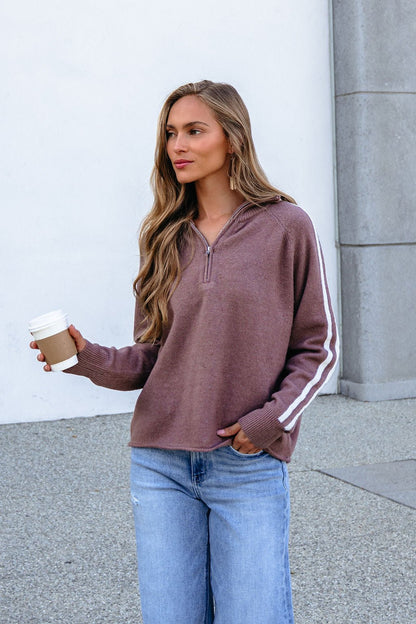 Woman in a Mocha Half Zip Collared Pullover holds a coffee cup while standing outside near a concrete wall.