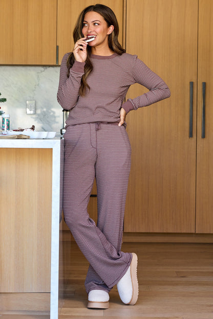 A woman wearing a Mocha Striped Long Sleeve Thermal Top smiles while eating a cookie in a modern kitchen.