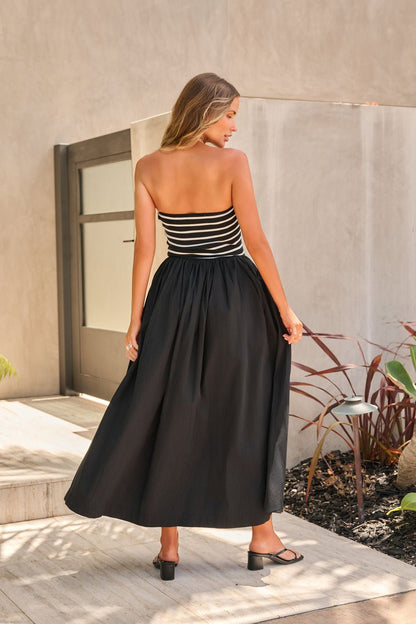 Woman in the Monaco Strapless Midi Dress in black, standing outdoors and facing away.