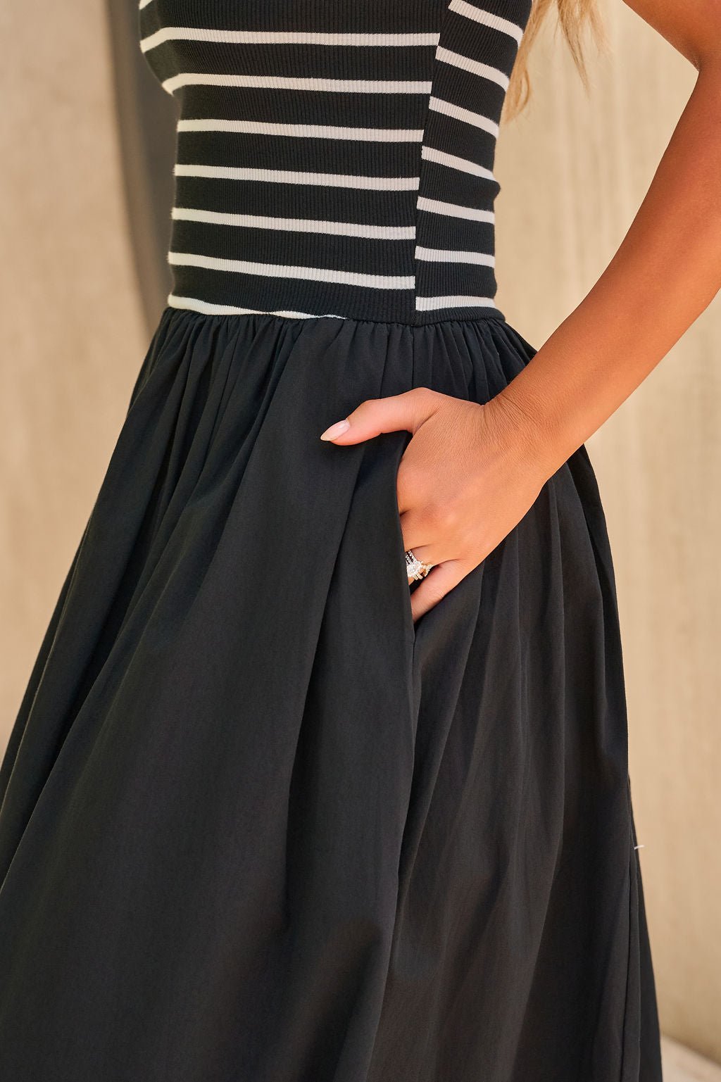 Woman wearing the Monaco Strapless Midi Dress in black, her hand casually tucked in the dress pocket.