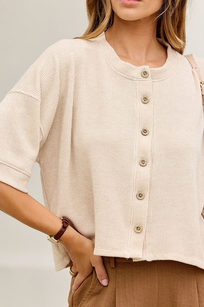 Woman wears the Monday Morning Button Down Top in oatmeal with brown pants and a watch on her left wrist.