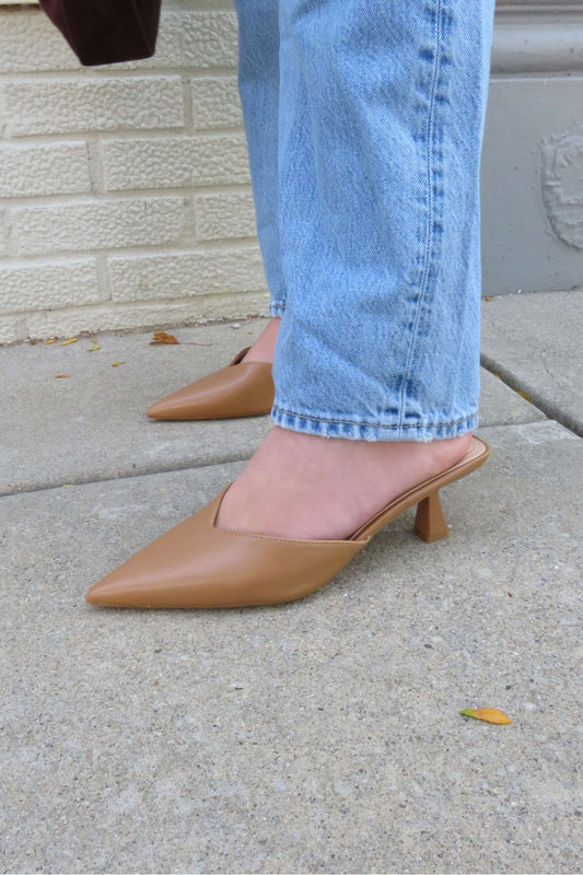 Wearing Morley Camel Open Back Kitten Heels - DOORBUSTER, person in light blue jeans stands on a sidewalk by a brick wall.