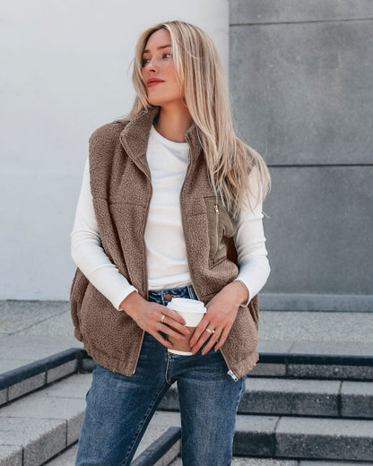 Woman in the Mountainside Zip Up Fleece Vest - Mocha, white shirt, and jeans holding coffee—perfect fall style on outdoor steps.