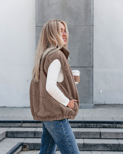 Woman with long blonde hair wears the Mountainside Zip Up Fleece Vest in Mocha and jeans, holding coffee—cozy fall style.