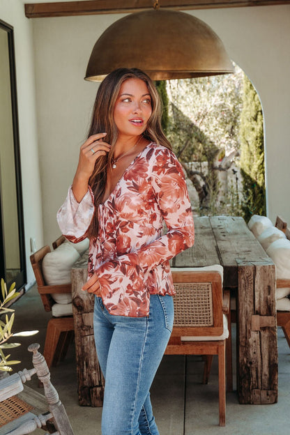 Woman in a Multi Brown Floral Mesh Top and jeans stands by a rustic patio table, looking to the side with a relaxed vibe.