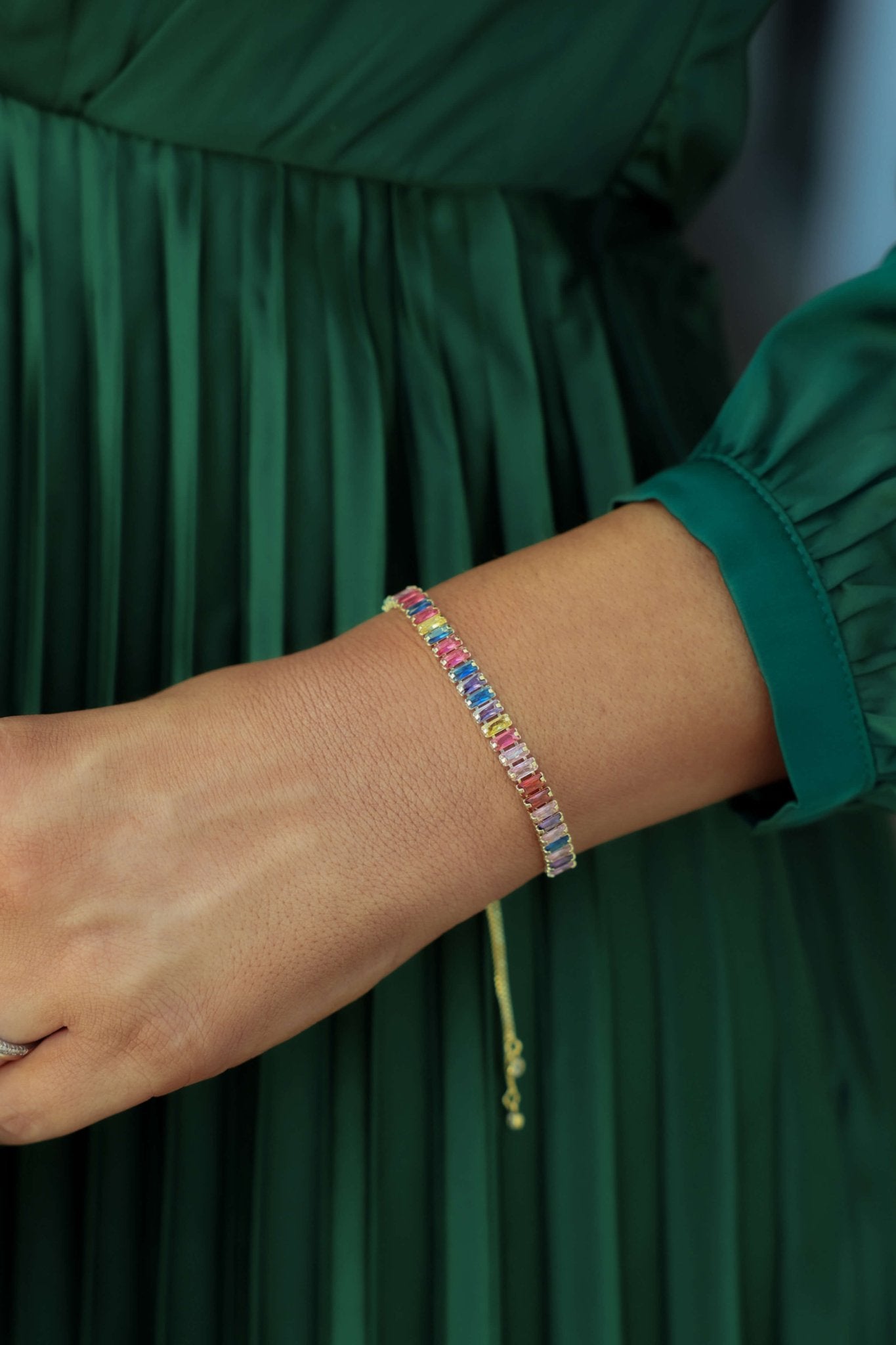 Wearing a green pleated dress, she styles the Multi Color Gem Bracelet—vibrant gems and an adjustable fit for comfort.