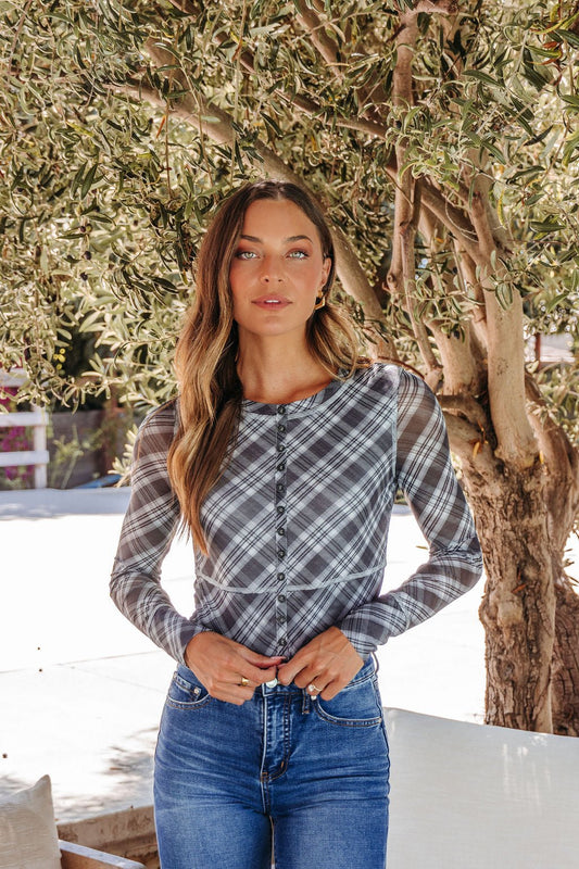 A woman with long wavy hair models the Multi Grey Plaid Mesh Top - DOORBUSTER outdoors by a leafy tree, confident and stylish.