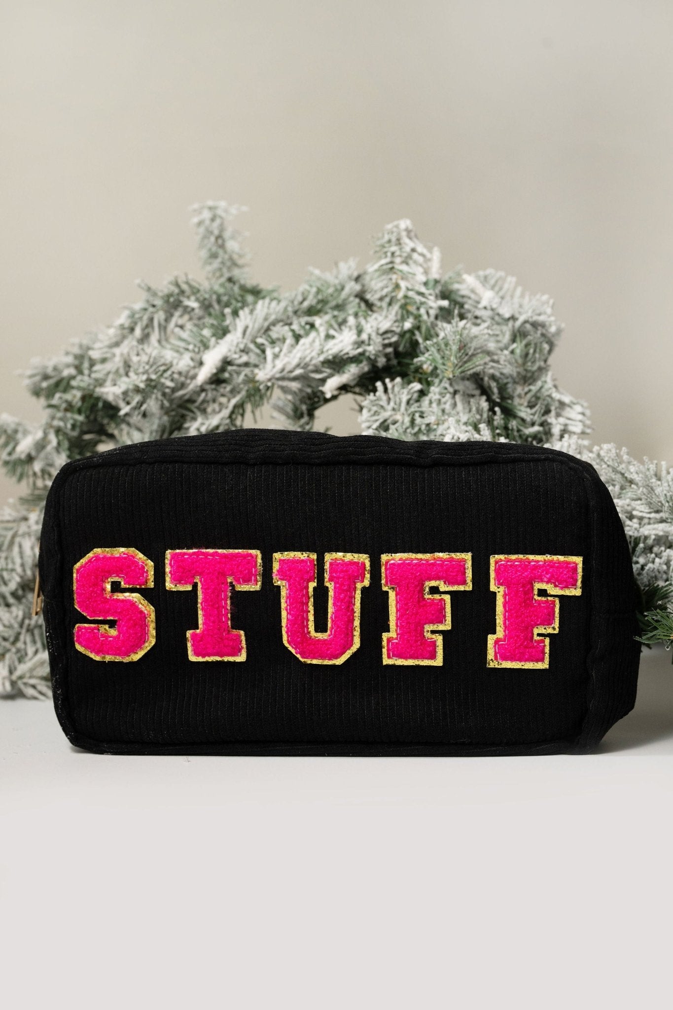 A black Multi Mix Patch Make Up Bag with bold pink and yellow STUFF lettering, shown in front of a frosted pine branch.