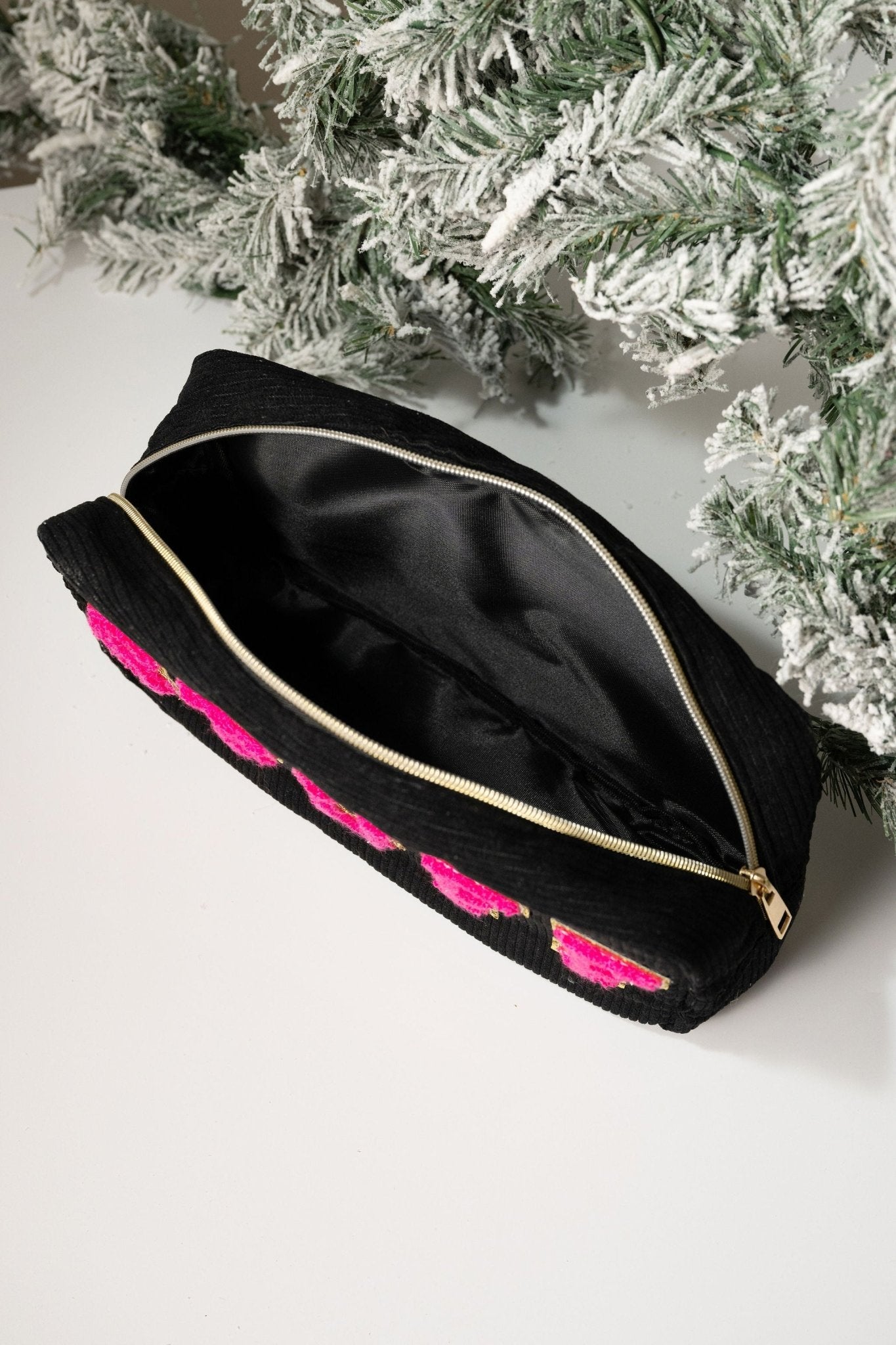 A Multi Mix Patch Make Up Bag with black zipper and pink accents sits open on a white surface near frosted evergreens.