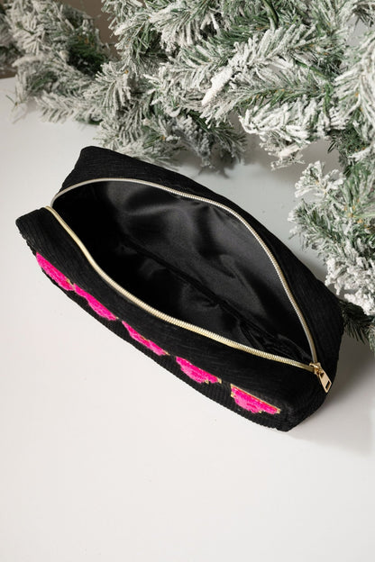 A Multi Mix Patch Make Up Bag with black zipper and pink accents sits open on a white surface near frosted evergreens.