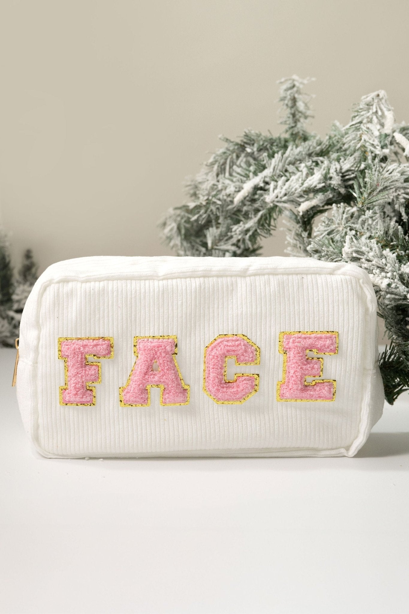 A Multi Mix Patch Make Up Bag with FACE in pink and gold letters, shown beside frosted evergreen branches.