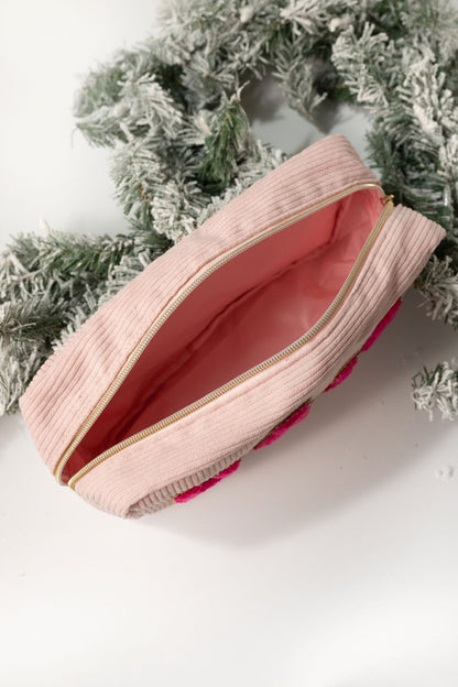 A Multi Mix Patch Make Up Bag with a light pink interior, placed near frosted green pine branches.