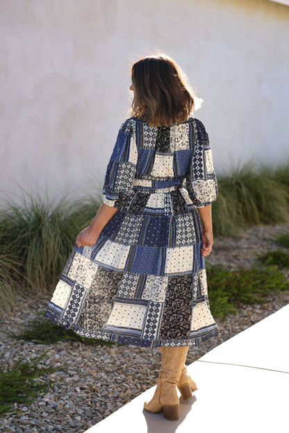 A woman in a Multi Navy Patch Print Midi Dress stands outdoors on a sunny day, facing away from the camera.