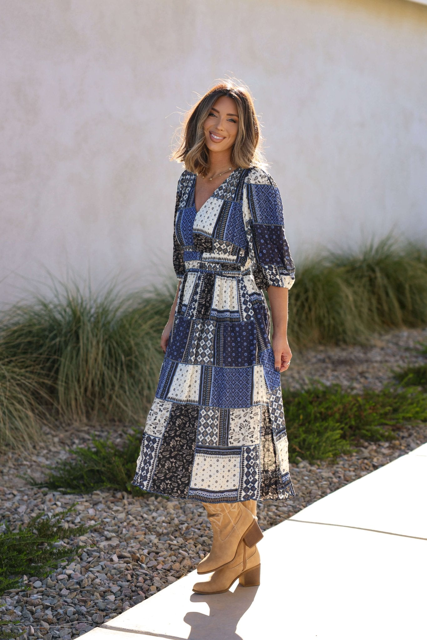 Smiling woman wears the Multi Navy Patch Print Midi Dress - FINAL SALE with tan boots, standing outside on a sidewalk.