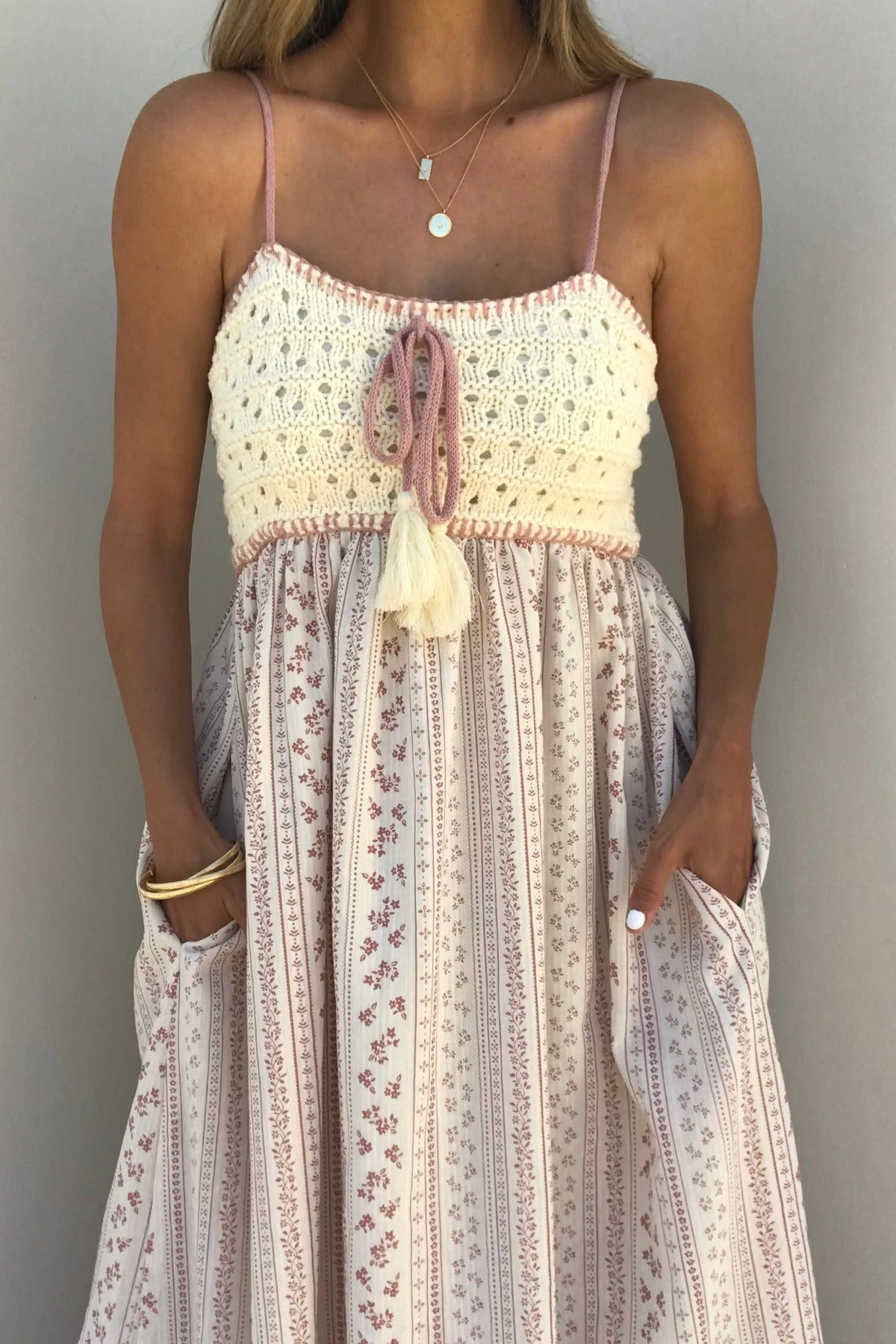 Woman in a Multi Pink Stripe Crochet Maxi Dress, layered necklaces, and gold bracelets against a plain background.