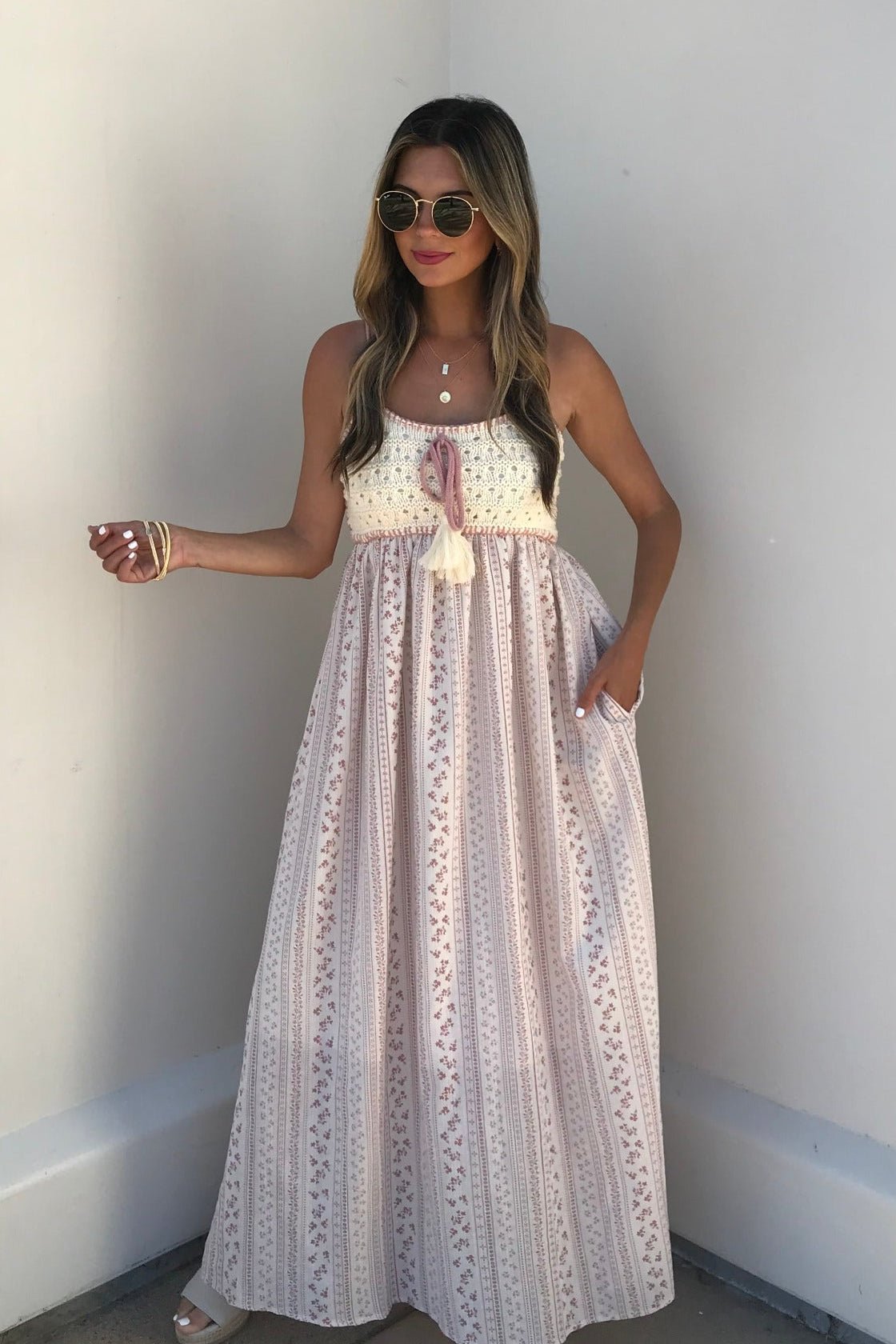 A woman in sunglasses wears the Multi Pink Stripe Crochet Maxi Dress, standing against a plain light-colored wall.