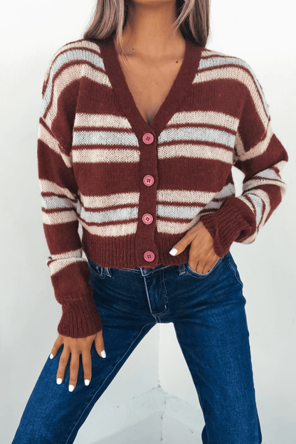 Woman wearing a Multi Striped Button Up Sweater Cardigan with pink buttons and blue jeans, posing with one hand in her pocket.