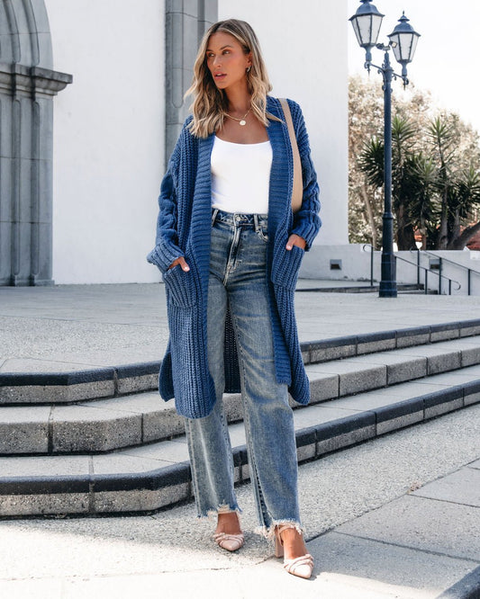 A woman wears the Muse By Magnolia Blue Chunky Duster Cardigan with a white top and jeans, standing on outdoor steps by a white building.