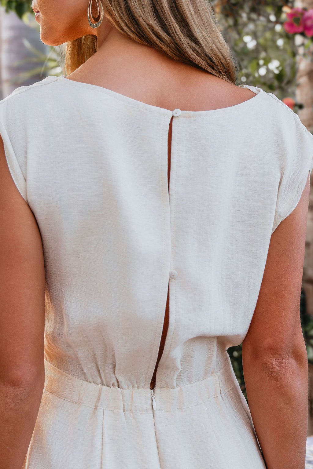 A woman in the Natural Belted Wide Leg Linen Jumpsuit, seen from the back, with a keyhole and adjustable waist.
