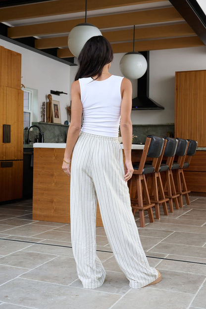 A woman wearing Natural Striped Linen Drawstring Pants stands in a modern kitchen, facing away from the camera.