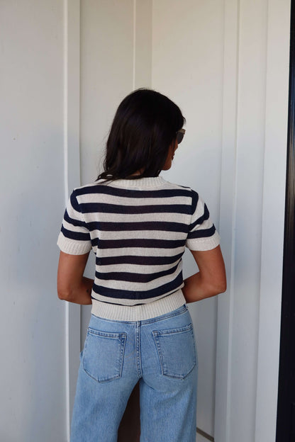 Woman with long dark hair wears a Navy and Cream Striped Short Sleeve Sweater and light blue jeans, back to the camera.