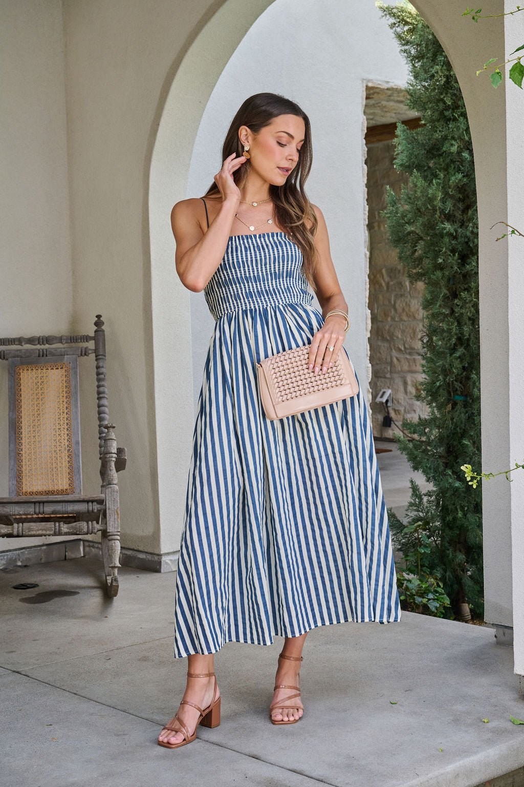 Woman in a Navy and Ivory Striped Midi Dress stands under an archway, paired with a beige clutch and heels.