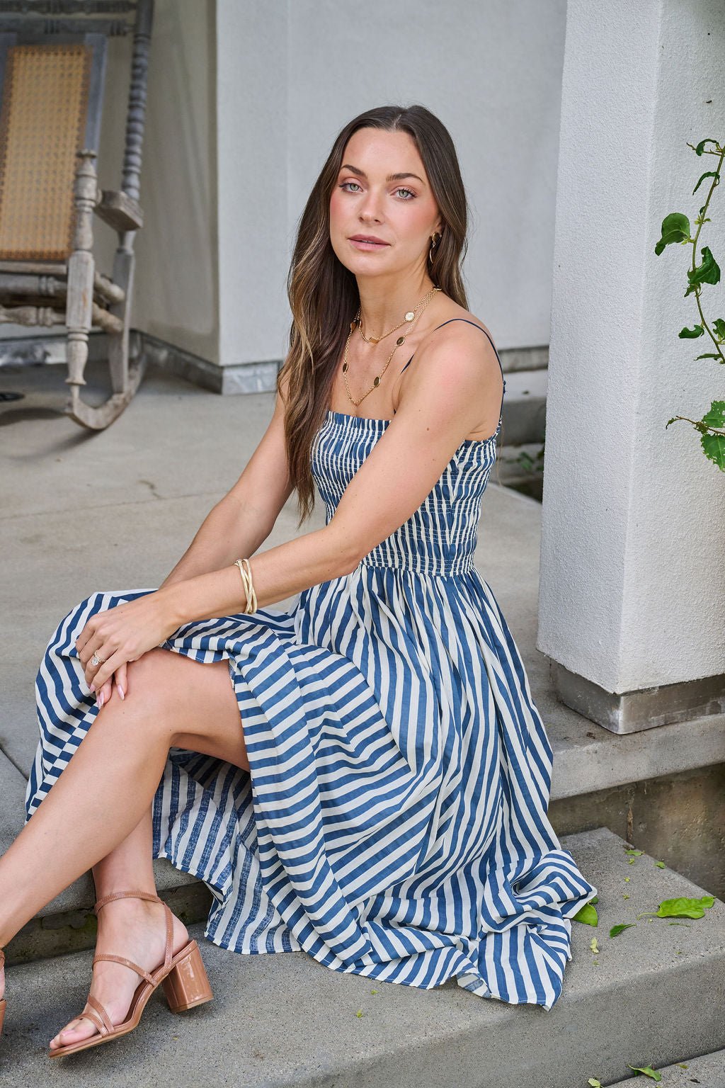 A woman in the Navy and Ivory Striped Midi Dress sits on steps, gazing at the camera with a relaxed expression.