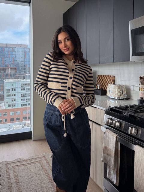 A woman wears the Navy and Tan Striped Button Down Cardigan - FINAL SALE in a modern kitchen with city views.