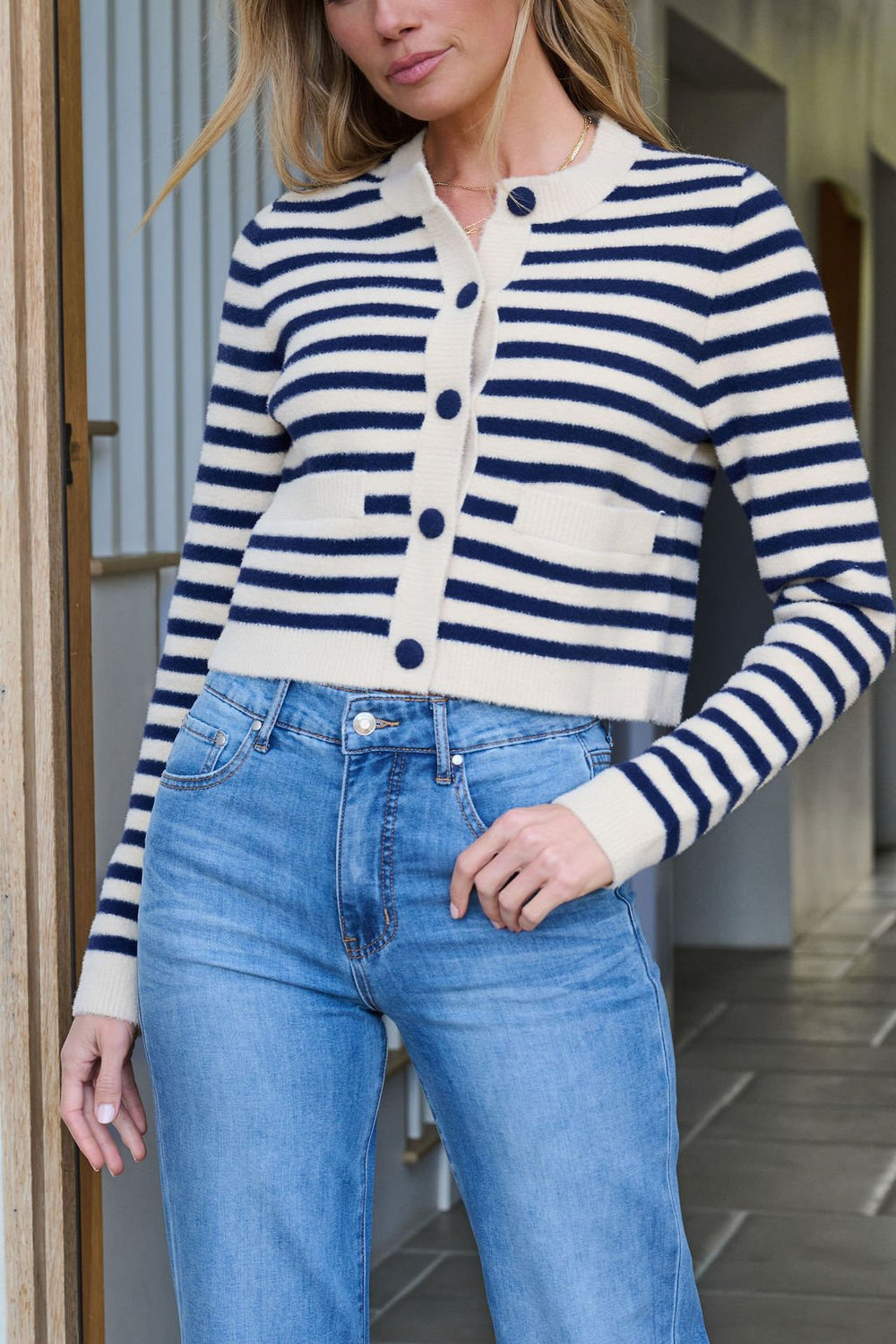 Model in Navy and Tan Striped Button Down Cardigan - FINAL SALE, paired with blue jeans, poses indoors with a hand on her hip.