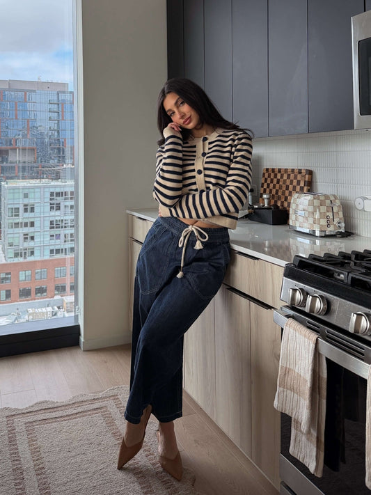 A woman in a Navy and Tan Striped Button Down Cardigan leans on a kitchen counter with city buildings visible through the window.