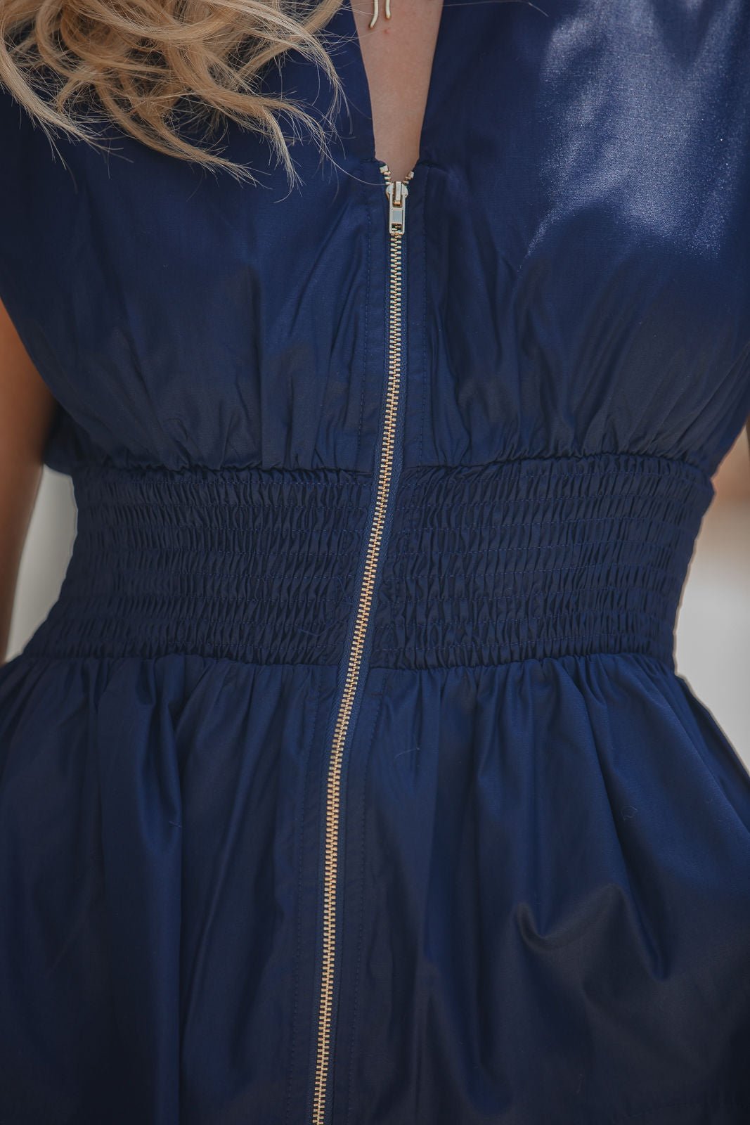 The Navy Zip Smocked Peplum Top features a zip front and ruched waist; image shows only torso and partial arm.