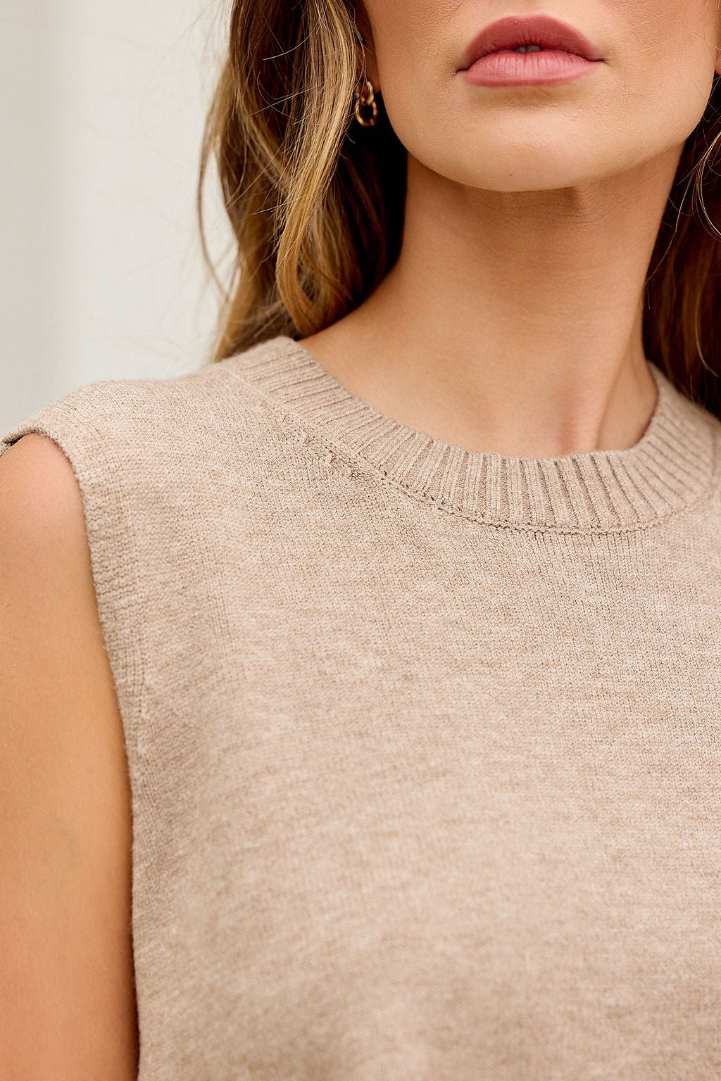 Woman in Nine To Five Cashmere Sweater - Dark Beige, sleeveless, relaxed fit, wavy hair, gold hoop earring; shown shoulder to lips.
