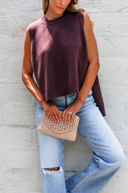 Woman in Nine To Five Cashmere Sweater - Mocha and ripped jeans holds a beige woven clutch against a light textured wall.