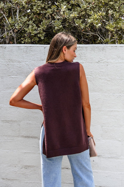 A woman in a relaxed fit Nine To Five Cashmere Sweater - Mocha and light jeans stands facing a white wall with plants above it.