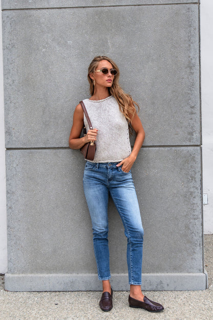 Woman in sunglasses, Free People Opal Tank Top, blue jeans, and loafers stands by a gray wall holding a brown shoulder bag.
