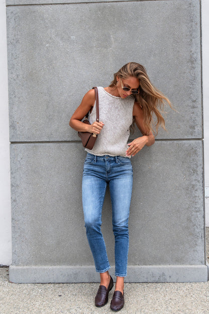 Woman in sunglasses, Free People Opal Tank Top, jeans, and loafers stands by a gray wall holding a brown shoulder bag.