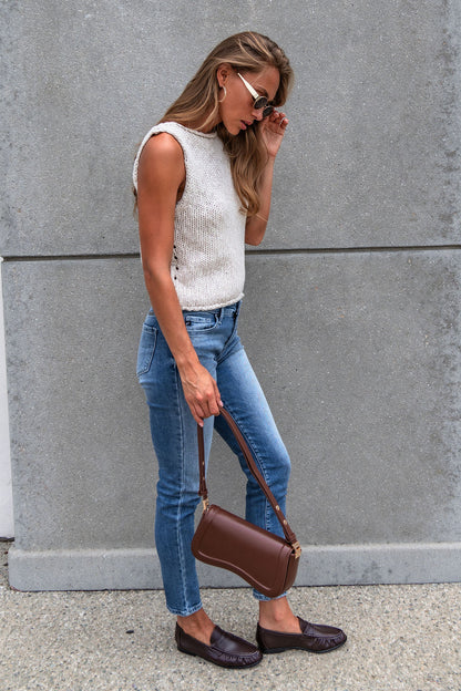 A woman in jeans, Free People Opal Tank Top, loafers, sunglasses, and a brown purse stands by a gray concrete wall.