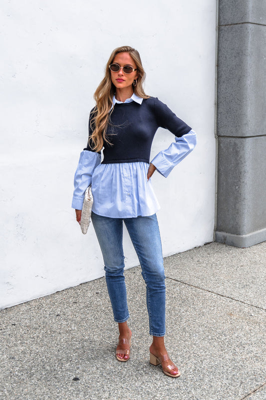 Woman in sunglasses, Steve Madden Lenny Top - Navy, jeans, and heels stands outdoors holding a beige clutch against a white wall.