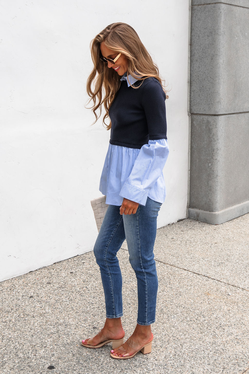 Woman in jeans and the Steve Madden Lenny Top - Navy smiles, holding a white clutch, standing against a white wall.